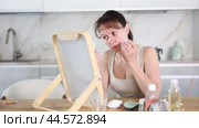 Careful middle-aged lady cleansing her face with round cotton discs while seated at a table in her house. Стоковое видео, видеограф Яков Филимонов / Фотобанк Лори