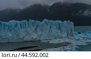 A wall of blue ice with cracks, sharp peaks rises above a glacial lake. Melted ice floes float in turquoise water. Coastal mountains in clouds, fog. Perito Moreno glacier. El Calafate. Argentina. Стоковое фото, фотограф Вера Ивановна Кубарева / Фотобанк Лори