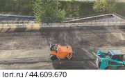 IRKUTSK, RUSSIA - September 06, 2024: Video of road works on the territory adjacent to a high-rise building. One worker brings crushed stone and sand on a loader, another worker compacts the soil with a roller. Редакционное видео, видеограф Виктория Катьянова / Фотобанк Лори