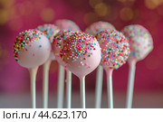 Colorful sprinkle-covered cake pops on pink background. Стоковое AI-изображение, AI-художник Иван Рябоконь / Фотобанк Лори