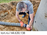 Worker connects perforated drain pipe to septic tank through which wastewater flows into leach field. Стоковое фото, фотограф Владимир Григорьев / Фотобанк Лори