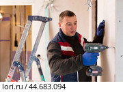 Male contractor engaged in drywall mounting using screw gun in overhauls indoors. Стоковое фото, фотограф Яков Филимонов / Фотобанк Лори