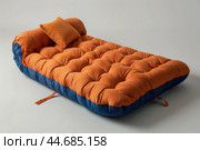 Orange futon mattress lying on grey background. Стоковое AI-изображение, AI-художник Иван Рябоконь / Фотобанк Лори