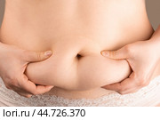 Woman hand holding excessive belly fat, overweight concept. woman with fat belly, overweight female body, close-up studio shot. concept of dieting, losing weight. Стоковое фото, фотограф Павел Муравьев / Фотобанк Лори