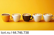Various hot coffees in ceramic cups lined up on a yellow background. Стоковое AI-изображение, AI-художник Veniamin Kraskov / Фотобанк Лори