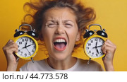 Stressed young woman screaming holding two alarm clocks on yellow background. Стоковое AI-видео, аниматор Юрий Поздников / Фотобанк Лори