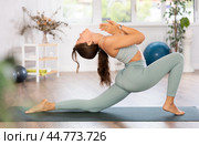 Young woman yoga trainer performing crescent lunge pose on black rug. Стоковое фото, фотограф Яков Филимонов / Фотобанк Лори