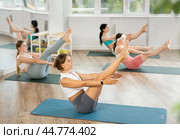 Young female participant working out Paripurna Navasana, boat pose with students group. Стоковое фото, фотограф Яков Филимонов / Фотобанк Лори