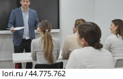 Young male teacher near interactive board, gesturing with hand while consecrating topic of lesson for adults in classroom. Стоковое видео, видеограф Яков Филимонов / Фотобанк Лори