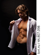 Handsome man advertising model in unbuttoned white shirt with abs muscle press posing in shadow at black studio shot. Portrait of stylish guy with perfect muscular sexy torso, pose. Copy ad text space. Стоковое фото, фотограф Aleksandr Golubev / Фотобанк Лори