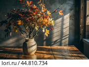 Branches with golden autumn leaves in a ceramic vase on a wooden table by the window. The concept of home comfort. Autumn decor for Halloween. Стоковое AI-изображение, AI-художник Photojuli / Фотобанк Лори