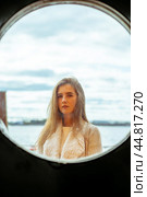 The face of young girl in round frame window on background of sea, ocean, on waterfront. Portrait in circle, backlit, vertical. Стоковое фото, фотограф Natalia Gdovskaia / Фотобанк Лори