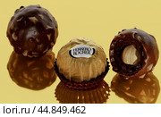 Ferrero rocher chocolate and hazelnut confectionery. chocolate consists of whole roasted hazelnut encased in thin wafer shell. golden mirror background (2023 год). Редакционное фото, фотограф Павел Муравьев / Фотобанк Лори