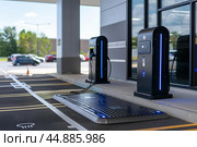 Electric vehicle charging station glowing blue at modern dealership. Стоковое AI-изображение, AI-художник Иван Рябоконь / Фотобанк Лори