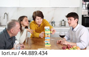 Elderly woman engrossed in playing jenga with husband, adult daughter and son-in-law during family gathering with wine at home, concentrating on extracting block without collapsing tower. Стоковое видео, видеограф Яков Филимонов / Фотобанк Лори