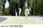 Young beautiful brunette girl in a beige dress walks in a summer city park. Стоковое видео, видеограф Андрей Аркуша / Фотобанк Лори