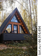 A-shaped frame house in Scandinavian style. The landscape. Quiet rest. The concept of glamping and chalet rentals. A wooden house with a veranda in nature around an autumn birch forest. Стоковое фото, фотограф Photojuli / Фотобанк Лори