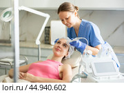 Female cosmetologist performing anti-aging face phototherapy procedure, shrink pores and repair damaged skin for young girl client in clinic of aesthetic medicine. Стоковое фото, фотограф Яков Филимонов / Фотобанк Лори