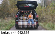A little girl is sitting in the trunk of a car and inflating an orange balloon for the Halloween holiday. The concept of children's Halloween. Стоковое видео, видеограф Терехова Марина / Фотобанк Лори