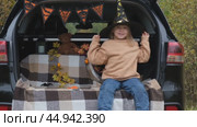 A little girl is sitting in the trunk of a car and wearing a witch hat for the Halloween holiday. The concept of children's Halloween. Стоковое видео, видеограф Терехова Марина / Фотобанк Лори