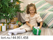 Christmas spirit. Happy little smiling girl opening gift box sitting on the floor near the Christmas tree. Happy girl unwrapping Christmas present looking in box. Holidays and celebrations concept. Стоковое фото, фотограф Ирина Михайличенко / Фотобанк Лори