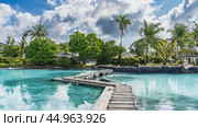 A winding concrete footpath crosses the swimming pool with clear turquoise water. In the distance, on the shore there is green tropical vegetation, palm trees, gazebos. Blue sky, clouds. Philippines. Стоковое фото, фотограф Вера Ивановна Кубарева / Фотобанк Лори