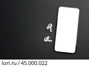 Modern smartphone with blank white screen with wireless earphones on black background. Mockup TWS earbuds with smartphone on black background. copy space. Стоковое фото, фотограф Павел Муравьев / Фотобанк Лори