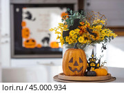 A vase of flowers, pumpkins and a scary castle with a witch on the background of a Scandi-style white kitchen interior. The concept of home and comfort. Autumn decor for Halloween. Стоковое фото, фотограф Photojuli / Фотобанк Лори