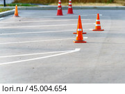 Vibrant orange traffic cones stand resolutely in a public parking lot, signaling caution and guiding drivers through a maze of potential hazards, reminding us to navigate safely. Стоковое фото, фотограф Татьяна Степанищева / Фотобанк Лори