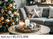 Cozy decor in gray and green tones in the interior of the Christmas room, candles, a Christmas tree decorated with crystal toys and garlands. A festive living room in the house. Стоковое AI-изображение, AI-художник Photojuli / Фотобанк Лори