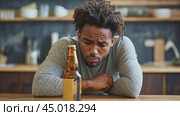 Young man is sitting at his kitchen table, looking sadly at a bottle of beer. Стоковое AI-видео, аниматор Юрий Поздников / Фотобанк Лори