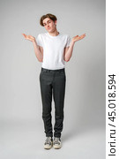 Young Man in Casual Attire Shrugging Shoulders Expressing Uncertainty in Studio. Стоковое фото, фотограф Сергей Толмачёв / Фотобанк Лори