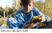 12-летний мальчик держит смартфон в зеленом чехле, пользуется интернетом, общается в чатах, прокручивает страницы на смартфоне. Солнечный день в парке. Стоковое видео, видеограф Яна Проничева / Фотобанк Лори