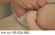 Close-up of a parent's hands changing a infant's nappy. Mum's hands fasten the nappy's velcro on the newborn's belly. Стоковое видео, видеограф Воловодов Владимир / Фотобанк Лори