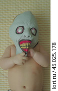 A child wearing a creepy monster mask with red gums and big teeth lies on his back. Small hands touch the mask and crumple it. The baby's shirt torso is visible. Creepy baby. Стоковое видео, видеограф Воловодов Владимир / Фотобанк Лори