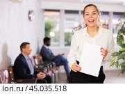 Friendly hostess woman stands at office reception with list of guests and expects invited visitors. Стоковое фото, фотограф Яков Филимонов / Фотобанк Лори