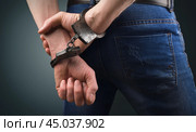 Arrested man stands handcuffed with his hands behind his back on a gray background. Стоковое фото, фотограф Дмитрий Кобзев / Фотобанк Лори