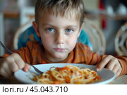 Young boy making a face while eating spaghetti with red sauce. Стоковое AI-изображение, AI-художник Иван Рябоконь / Фотобанк Лори