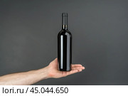 Sommelier hand holding red wine bottle on gray background. Стоковое AI-изображение, AI-художник Иван Рябоконь / Фотобанк Лори