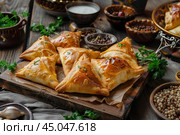 Delicious samsa or sambousak on wooden cutting board with spices and yogurt in bowls. Стоковое AI-изображение, AI-художник Иван Рябоконь / Фотобанк Лори