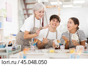 Senior woman assisting happy guy and girl painting ceramic mugs in workshop. Стоковое фото, фотограф Яков Филимонов / Фотобанк Лори