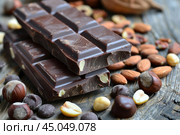 Two bars of dark chocolate with hazelnuts and almonds on wooden table. Стоковое AI-изображение, AI-художник Иван Рябоконь / Фотобанк Лори