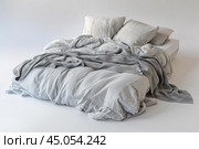 Unmade bed with grey linen bedding on white background. Стоковое AI-изображение, AI-художник Иван Рябоконь / Фотобанк Лори