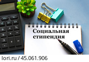 СОЦИАЛЬНАЯ СТИПЕНДИЯ - слова в белом блокноте на фоне калькулятора и зажимов. Стоковое фото, фотограф Жанна Гапанович / Фотобанк Лори