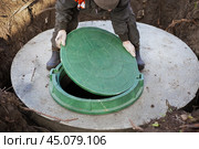 A worker installs a sewer manhole on a septic tank made of concrete rings. Construction of sewerage networks for country houses. Стоковое фото, фотограф Коханова Наталья / Фотобанк Лори