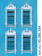 Close up view on a facade of ancient blue building with four windows with carved white stone platbands as texture (vertical orientation) (2018 год). Стоковое фото, фотограф Михаил Строгалев / Фотобанк Лори