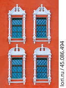 Close up view on a facade of ancient red building with four windows with carved white stone platbands  as texture (vertical orientation) Стоковое фото, фотограф Михаил Строгалев / Фотобанк Лори