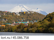 Город Петропавловск-Камчатский, Камчатский край, Россия. Красивый осенний городской пейзаж. Вид на здания на склоне холма. Вдалеке вулкан Авачинская Сопка. На переднем плане озеро Култучное. Путешествие на Камчатку. Дальний Восток России. Стоковое фото, фотограф Андрей Степанов / Фотобанк Лори