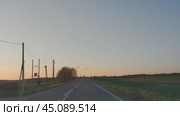 Дорога среди полей. Весенний ясный вечер, солнце низко у горизонта. Сельская асфальтовая дорога проходит среди полей с зеленой травой. По краям дороги встречаются деревья, кусты, столбы. Стоковое видео, видеограф Andrew_Swarga / Фотобанк Лори