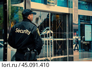 A uniformed security officer stands guard near the exit of the building on the street. Стоковое AI-изображение, AI-художник Ярославский Максим / Фотобанк Лори